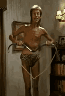 a shirtless man in leopard print underwear is standing on a treadmill in a living room .