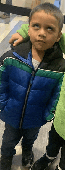 a young boy wearing a blue and green jacket looks up at the camera .