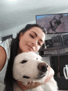 a woman is holding a white dog in front of a samsung television