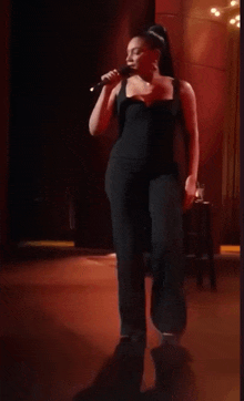 a woman in a black jumpsuit is singing into a microphone on a stage