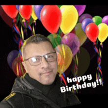 a man wearing glasses stands in front of balloons with the words happy birthday on the bottom