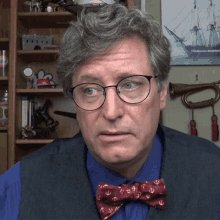 a man wearing glasses and a bow tie stands in front of a shelf with a picture of a ship on it