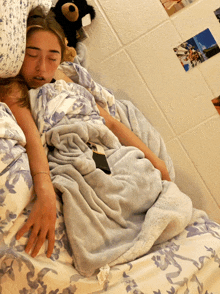 a girl is sleeping on a bed with a teddy bear and pictures on the wall behind her