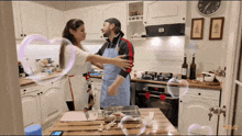 a man and a woman are hugging in a kitchen with a clock on the wall that shows the time as 2:30