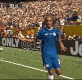 a soccer player in a blue jersey stands on a field in front of a sign that says " only one "