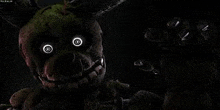 springtrap from five nights at freddy 's 3 is looking at the camera with glowing eyes in the dark .