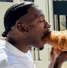 a man in a white shirt is eating a croissant with his mouth .