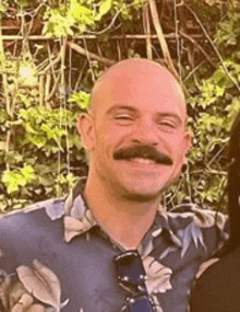 a bald man with a mustache is smiling for the camera while standing next to a woman .