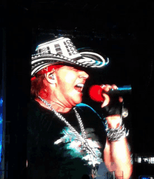 a man singing into a microphone wearing a cowboy hat that says guns n ' roses