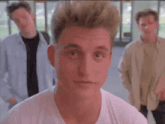 a man in a white shirt is looking at the camera with two other men behind him