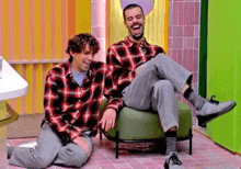 two men in plaid shirts are laughing and one is holding the other 's legs