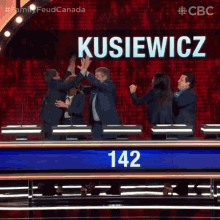 a group of people giving each other a high five in front of a sign that says kusiewicz 142