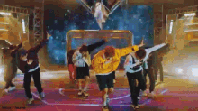 a group of young men are dancing on a stage in front of a basketball goal .