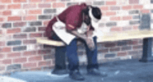 a man is sitting on a bench in front of a brick wall with his head down .