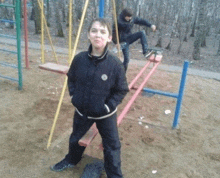 a boy in a black jacket is standing on a red seesaw