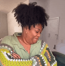 a woman with curly hair is wearing a crocheted sweater and making a funny face .