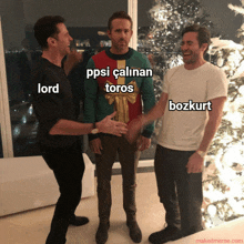 three men are standing in front of a christmas tree and one of them is wearing a sweater that says lord on it