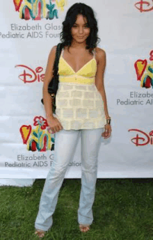 a woman wearing a yellow tank top and blue jeans is standing in front of a disney poster .