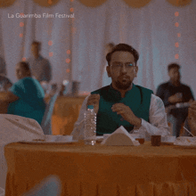 a man sitting at a table with a bottle of water in front of him and the words la guarimba film festival below him