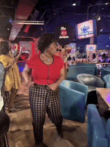 a woman in a red shirt is dancing in a room with a sign that says the sample