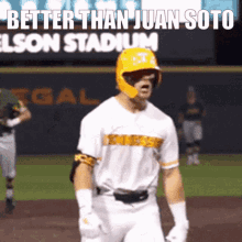 a baseball player wearing a yellow helmet stands on the field with the words better than juan soto in the background