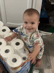 a baby stands next to a stack of toilet paper