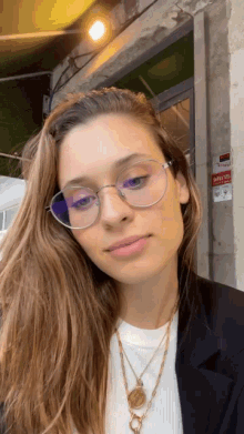 a woman wearing glasses and a necklace is standing in front of a building that has a sign on it that says safety