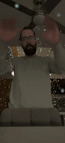 a man with a beard and glasses stands in front of a ceiling fan