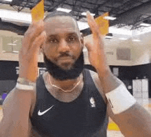 lebron james is wearing a black tank top and a necklace while standing on a basketball court .