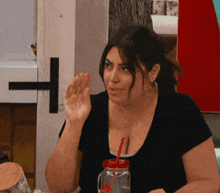 a woman sitting at a table with a mason jar with a red straw