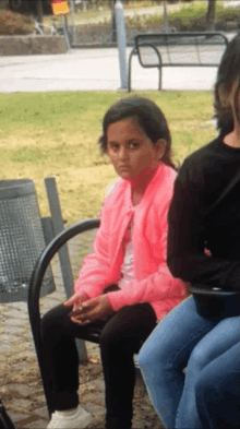 a girl wearing a pink jacket sits on a bench