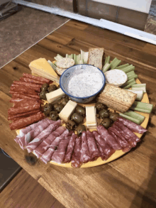 a tray of meats cheeses crackers olives and celery with a bowl of dipping sauce