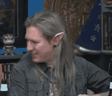 a man with long hair and elf ears is sitting at a table and saying `` you 're a wee pyromaniac '' .