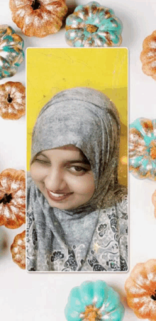 a woman wearing a hijab is surrounded by pumpkins on a yellow background