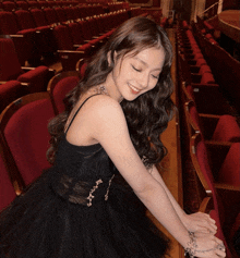 a woman in a black dress is smiling in an auditorium with red seats