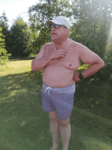 a shirtless man wearing plaid swim trunks and a hat