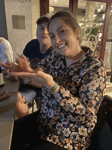 a woman in a floral shirt is smiling while sitting at a table