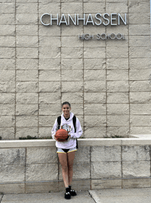 a girl stands in front of chanhassen high school holding a basketball