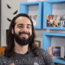 a man with long hair and a beard is smiling in front of a blue shelf with a book called ninho on it