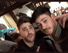 two men are posing for a picture in front of a bar with bottles of alcohol on the shelf behind them