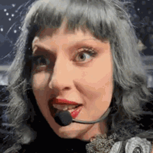 a woman with gray hair and red lips is wearing a microphone on her head .