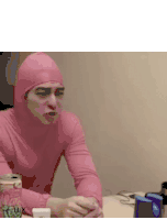 a man in a pink costume is sitting at a table with a can of soda .