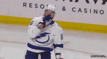 a hockey player wearing a helmet and gloves is standing on the ice with his hand on his chin .