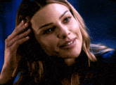 a woman in a blue shirt is smiling and touching her hair