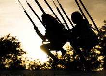 two girls are swinging on a swing set with the sun setting in the background