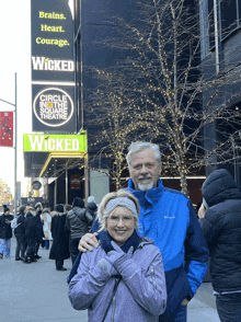 a man and woman standing in front of a wicked theater