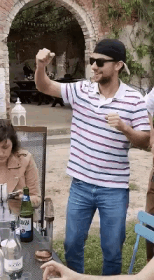 a man wearing a striped shirt and sunglasses is standing in front of a table with a bottle of wodka on it