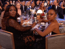 two women sit at a table with a bottle of campari in the background