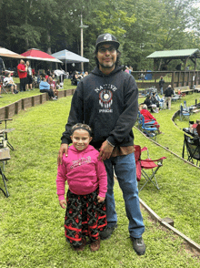 a man wearing a black native pride hoodie stands next to a little girl