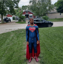 a man in a superman costume stands in a grassy yard